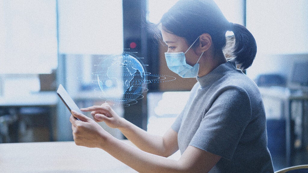 Woman wearing a facemask using a tablet that projects a holographic image of the Earth. Image credit: dowell/Getty Images